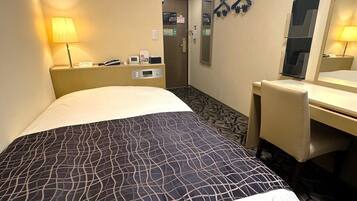 A hotel room with a bed, a desk, a chair, a lamp, a mirror, and a door.