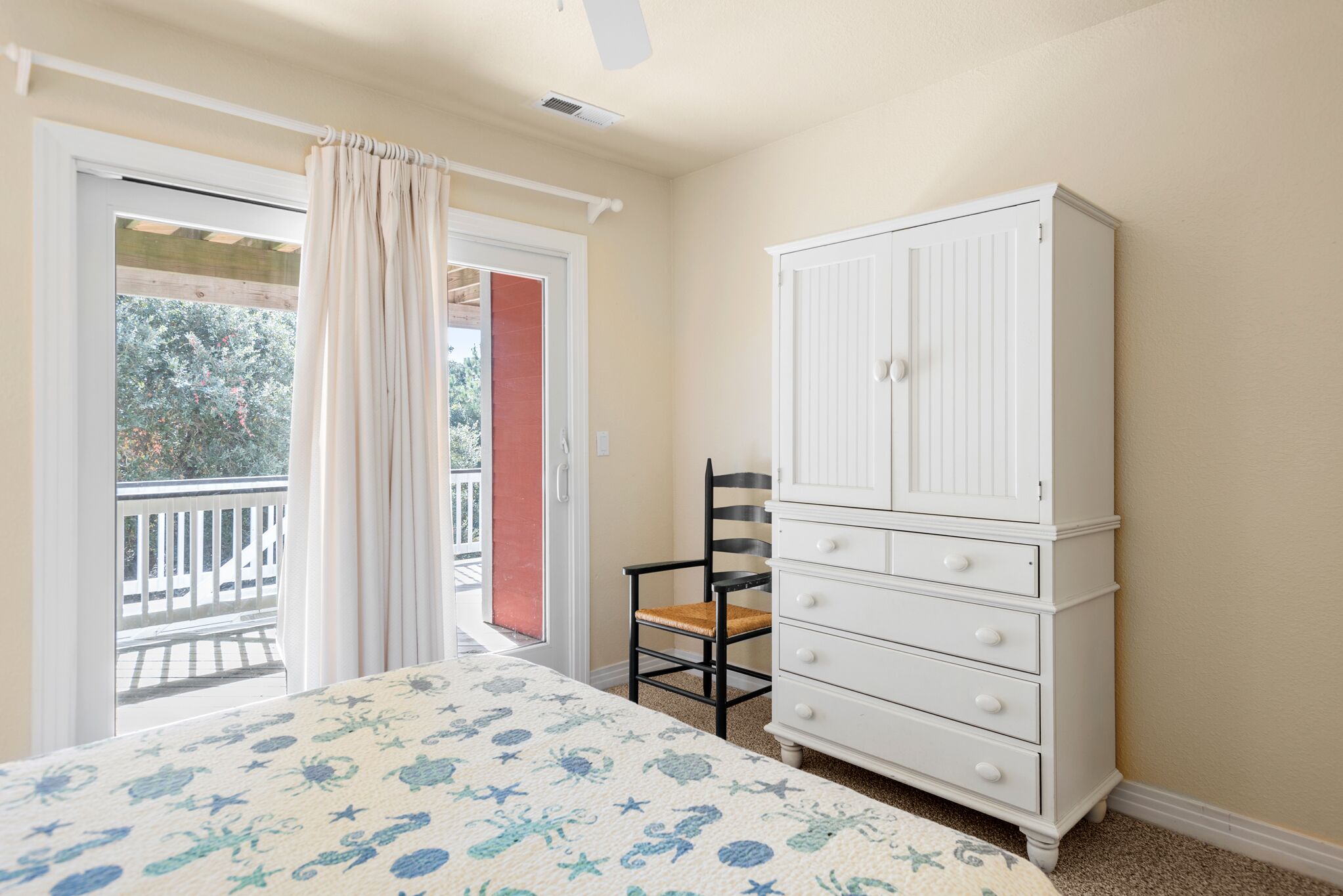 Une chambre à coucher avec un lit, une commode blanche, une chaise et une porte-fenêtre donnant sur un balcon.