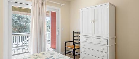 Une chambre à coucher avec un lit, une commode blanche, une chaise et une porte-fenêtre donnant sur un balcon.
