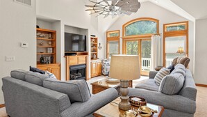 A spacious living room with a fireplace, a large TV, and a ceiling fan. - The Tipsea Turtle: Pool, & Hot Tub (Corolla)