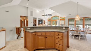 A spacious kitchen with a large island, wooden cabinets, and a dining area with a table and chairs. - The Tipsea Turtle: Pool, & Hot Tub (Corolla)