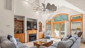 A spacious living room with a fireplace, built-in shelves, and a large window with a view of the outdoors. - The Tipsea Turtle: Pool, & Hot Tub (Corolla)