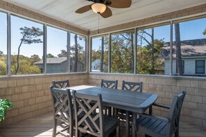 Eine überdachte Terrasse mit Tisch und Stühlen, großen Fenstern und einem Deckenventilator.