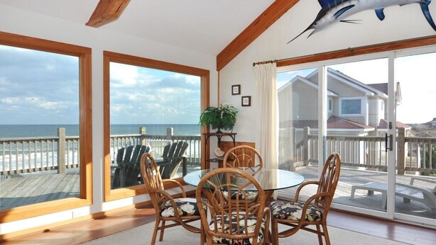 A room with a large glass door leading to a balcony, a wooden ceiling, and a view of the ocean. - Merry Winds: Oceanfront, Shared Pool, Great Views (Corolla)