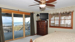 A bedroom with a bed, a ceiling fan, a television, a dresser, and a view of the ocean through a sliding glass door. - Merry Winds: Oceanfront, Shared Pool, Great Views (Corolla)