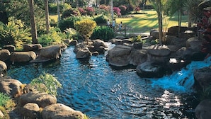 A serene garden with a small stream, large rocks, and palm trees.
