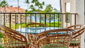 A glass table with wicker chairs, a balcony railing, and a view of palm trees and buildings.