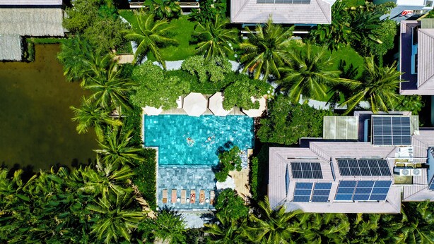An aerial view of a resort with a swimming pool surrounded by palm trees, solar panels, and a small pond. - Hoi An Eco Lodge & Spa (Da Nang)