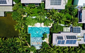 An aerial view of a resort with a swimming pool surrounded by palm trees, solar panels, and a small pond. - Hoi An Eco Lodge & Spa (Da Nang)