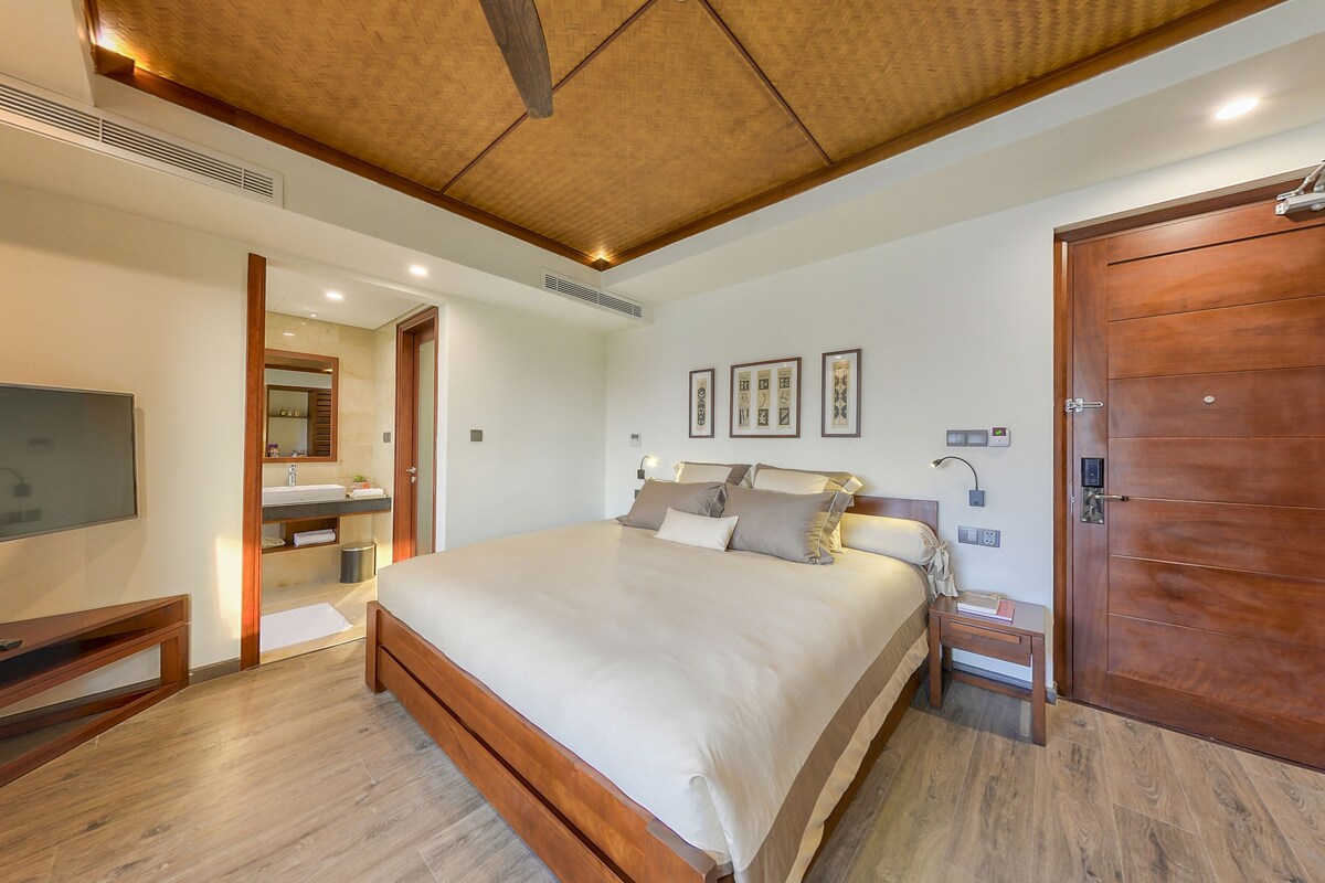 A modern bedroom with a large bed, wooden headboard, bedside tables, a TV, and a wardrobe.