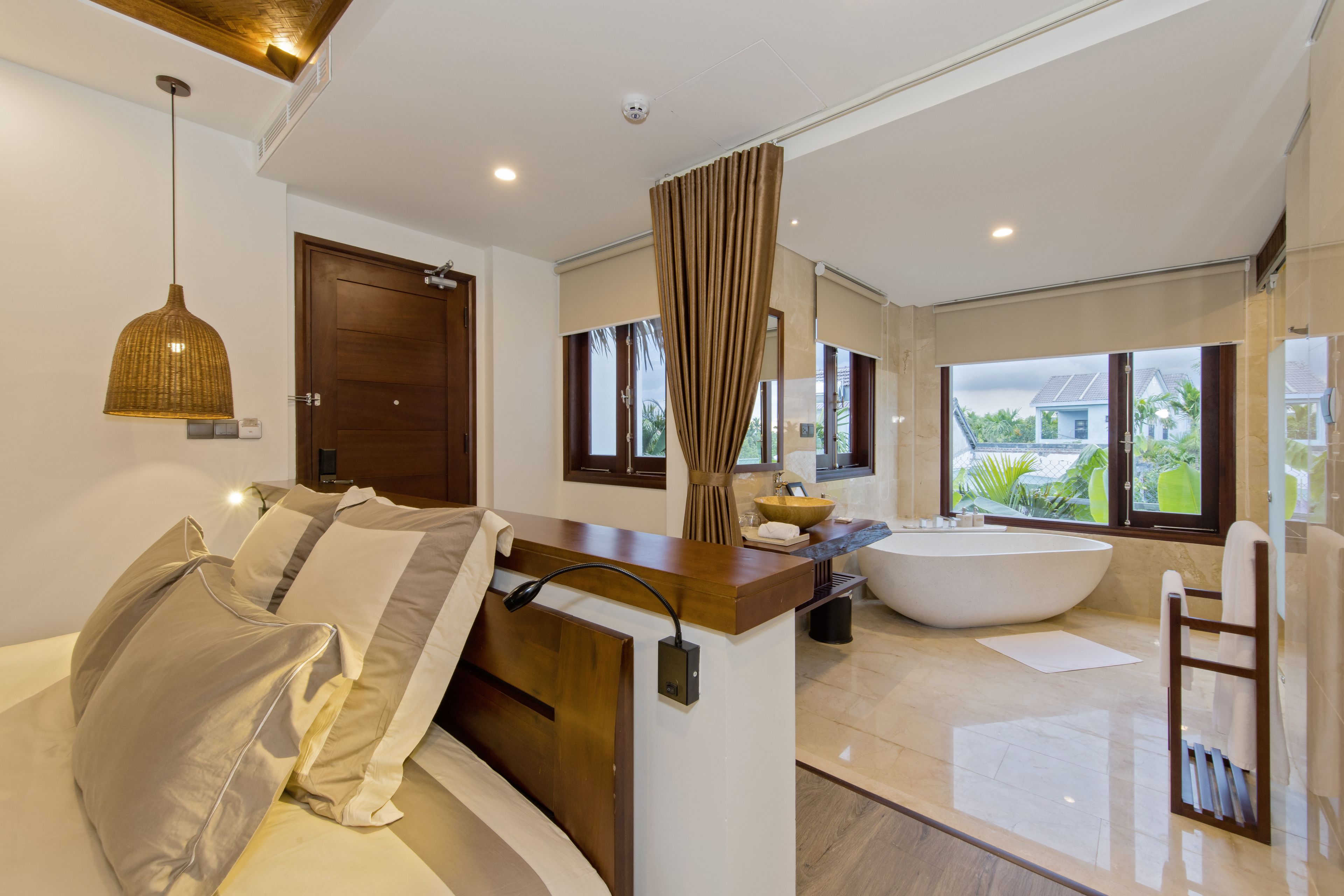 A modern bathroom with a freestanding bathtub, a wooden vanity, and a large window offering a view of the outdoors.