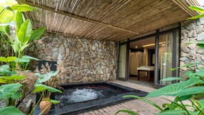 A spa area with a stone wall, a hot tub, and lush greenery. - Hoi An Eco Lodge & Spa (Da Nang)