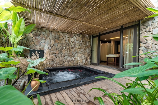 Un espace de bien-être doté d’un mur en pierre, d’un bain à remous et d’une végétation luxuriante.