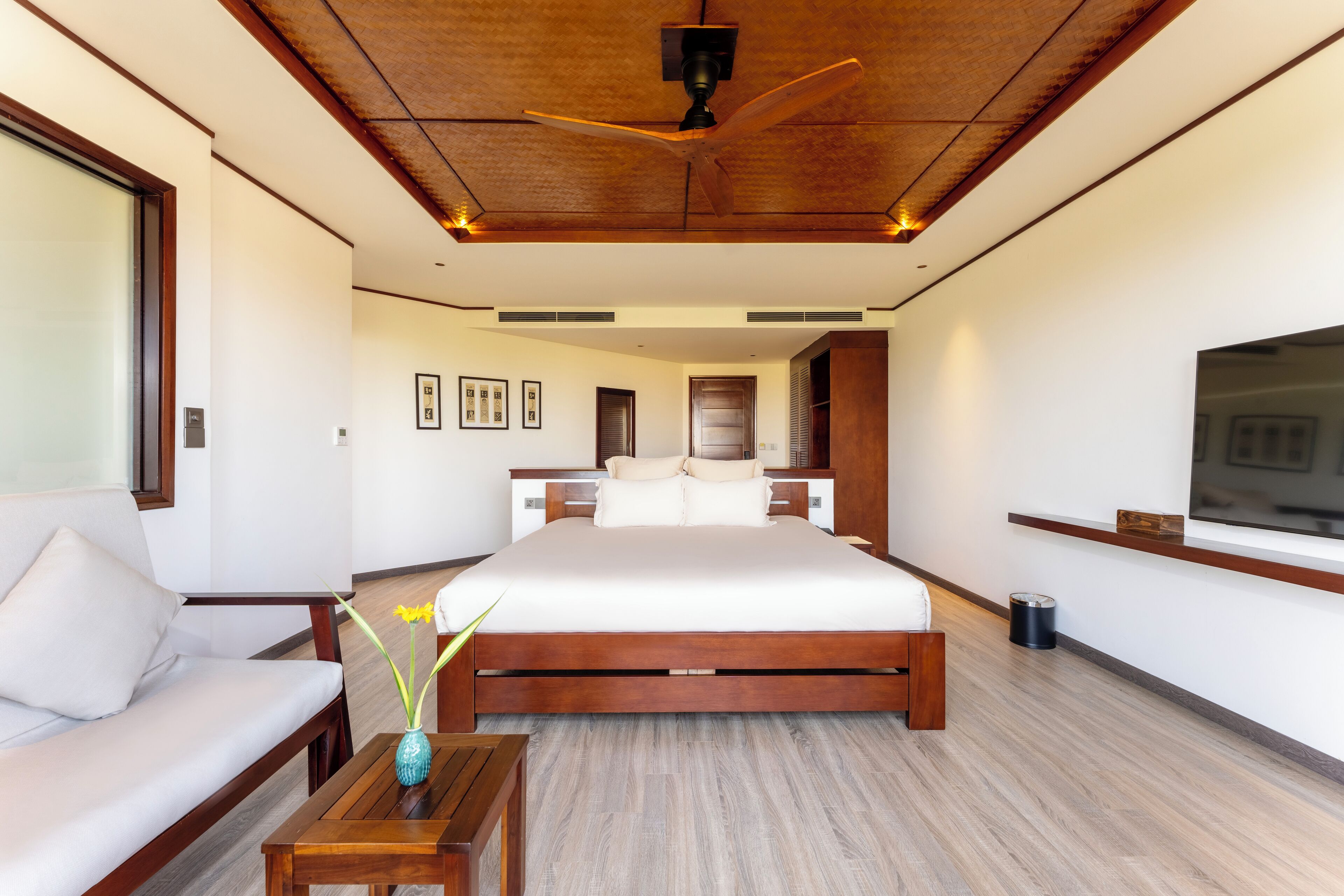 A modern hotel room with a large bed, a sofa, a wooden coffee table, and a ceiling fan.