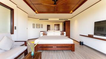 A modern hotel room with a large bed, a sofa, a wooden coffee table, and a ceiling fan.