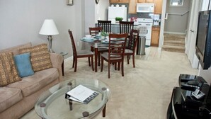 Una sala de estar con una mesa de centro de vidrio, un sofá y una zona de comedor con sillas y una mesa de madera.