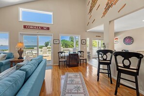 A spacious living area with a view of the ocean, a sign reading 'COROLLA NC', and a wooden floor.