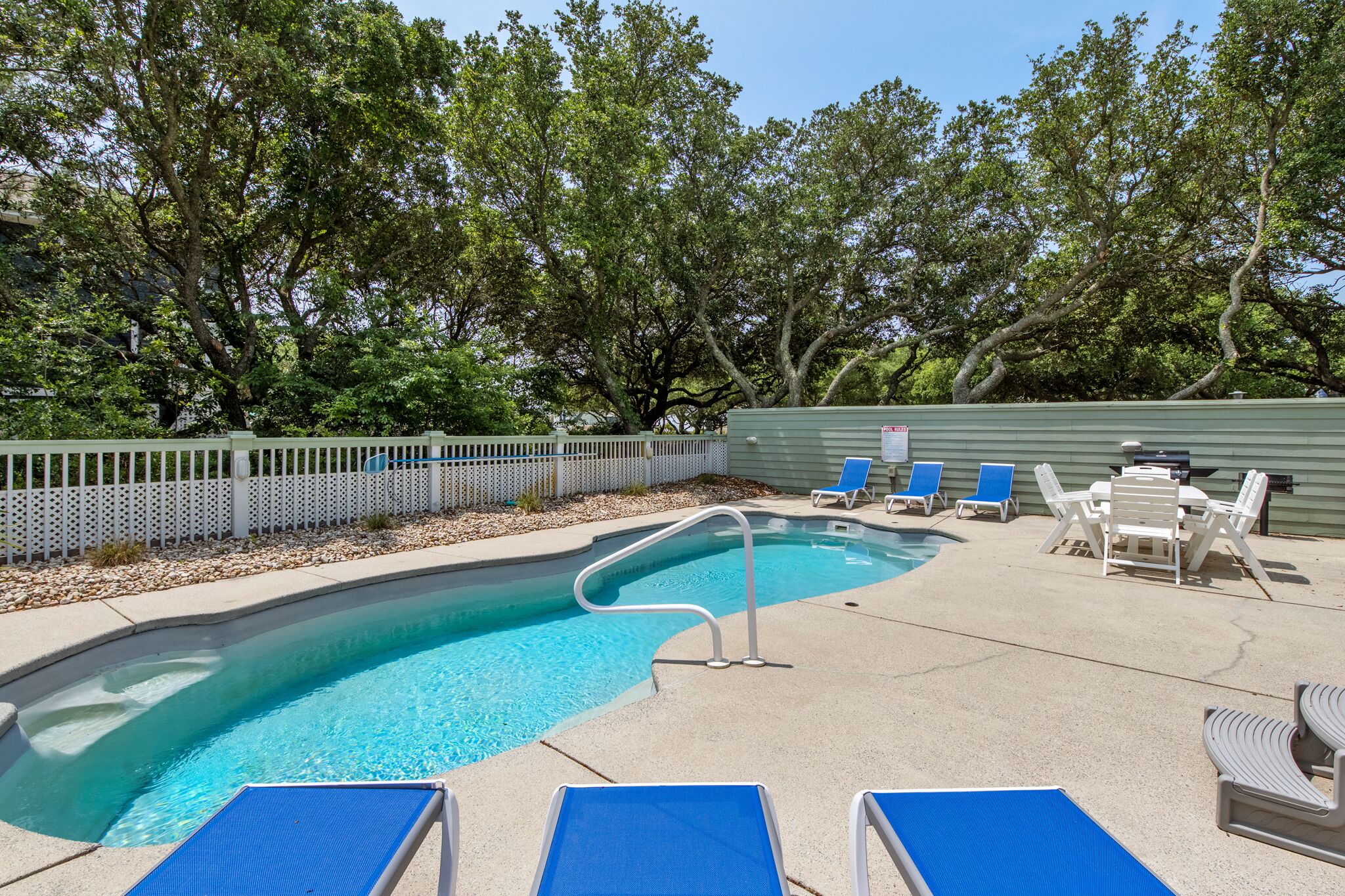 A swimming pool with a pool ladder, blue lounge chairs, and a table with chairs.