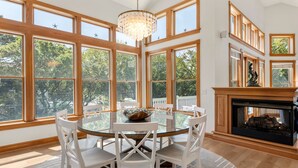 A dining area with a round glass table and white chairs, large windows, and a fireplace. - Always Summer: Private Pool, Spa, Club Access (Corolla)