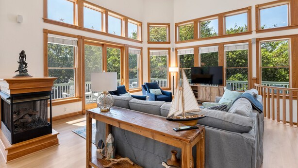 A spacious living room with large windows, a fireplace, a television, and a sailboat model. - Always Summer: Private Pool, Spa, Club Access (Corolla)