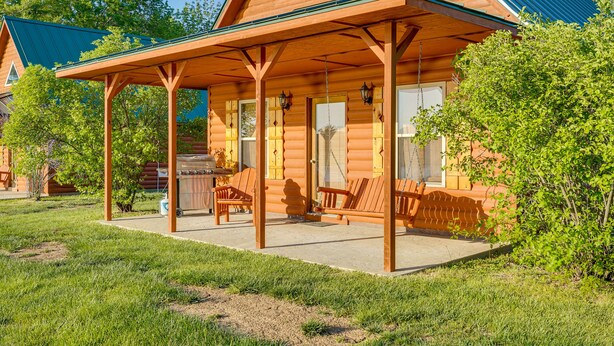 Eine Blockhütte mit verdeckter Veranda, Sitzgelegenheiten im Freien und Grillplatz.