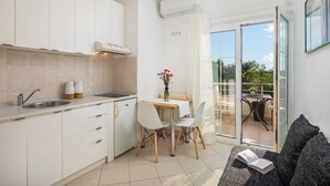 A modern kitchen with white cabinets, a sink, and a dining area with a table and chairs. There is a balcony with a table and chairs, and a sofa with a book. - Apartment Arausa with Pool II (Vodice)