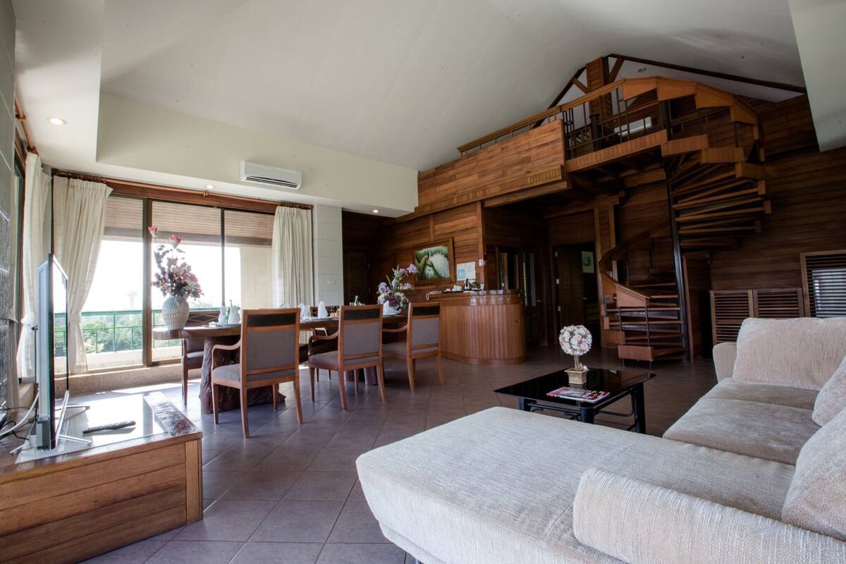 Ein geräumiger Wohnbereich mit hoher Decke, einer Holztreppe und einem Essbereich mit Stühlen und Tisch.