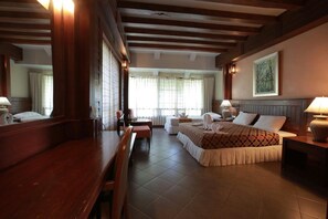 A hotel room with a large bed, a desk, a chair, a small table, and a window with curtains.
