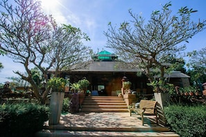 A building with a green roof, surrounded by trees and potted plants.