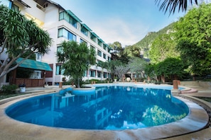 Ein Pool, umgeben von einem angelegten Garten mit Palmen und einem Gebäude im modernen Stil.