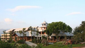 A multi-story hotel with a central tower, surrounded by lush greenery and a clear sky. - Khaoyai Fahsai Resort (Pak Chong)