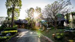 A pathway leading to a building with a traditional roof, surrounded by trees and a garden. - Khaoyai Fahsai Resort (Pak Chong)