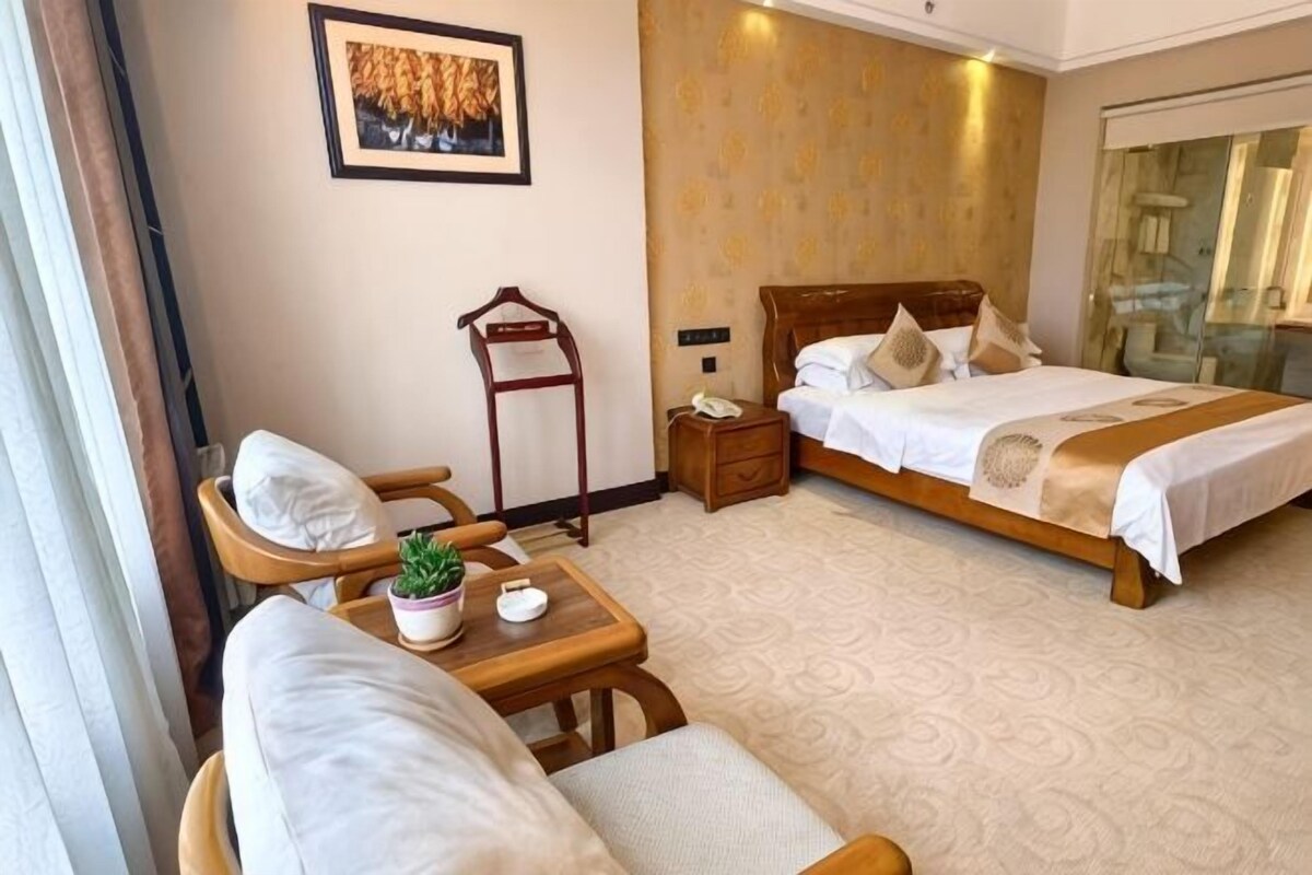 A hotel room with a bed, a chair, a small table with a plant, a nightstand, and a mirror.