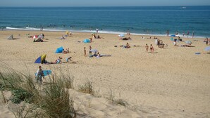 A sandy beach with people sunbathing and swimming, umbrellas, and a clear blue sky. - Villa 13 by Avecoeur (Saint-Augustin)