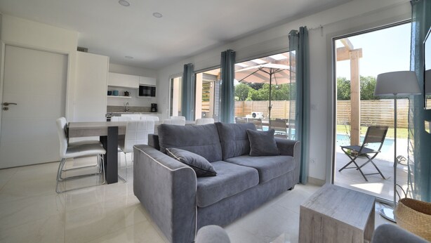 A modern living room with a grey sofa, a wooden coffee table, and a kitchen area with white cabinets and a microwave. - Villa 13 by Avecoeur (Saint-Augustin)