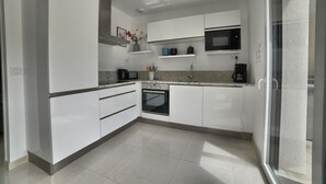 A modern kitchen with white cabinets, a built-in oven, a microwave, and a coffee maker. - Villa 13 by Avecoeur (Saint-Augustin)