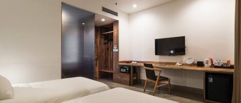 Een hotelkamer met twee bedden, een bureau met stoel, een televisie en een kleine koelkast.
