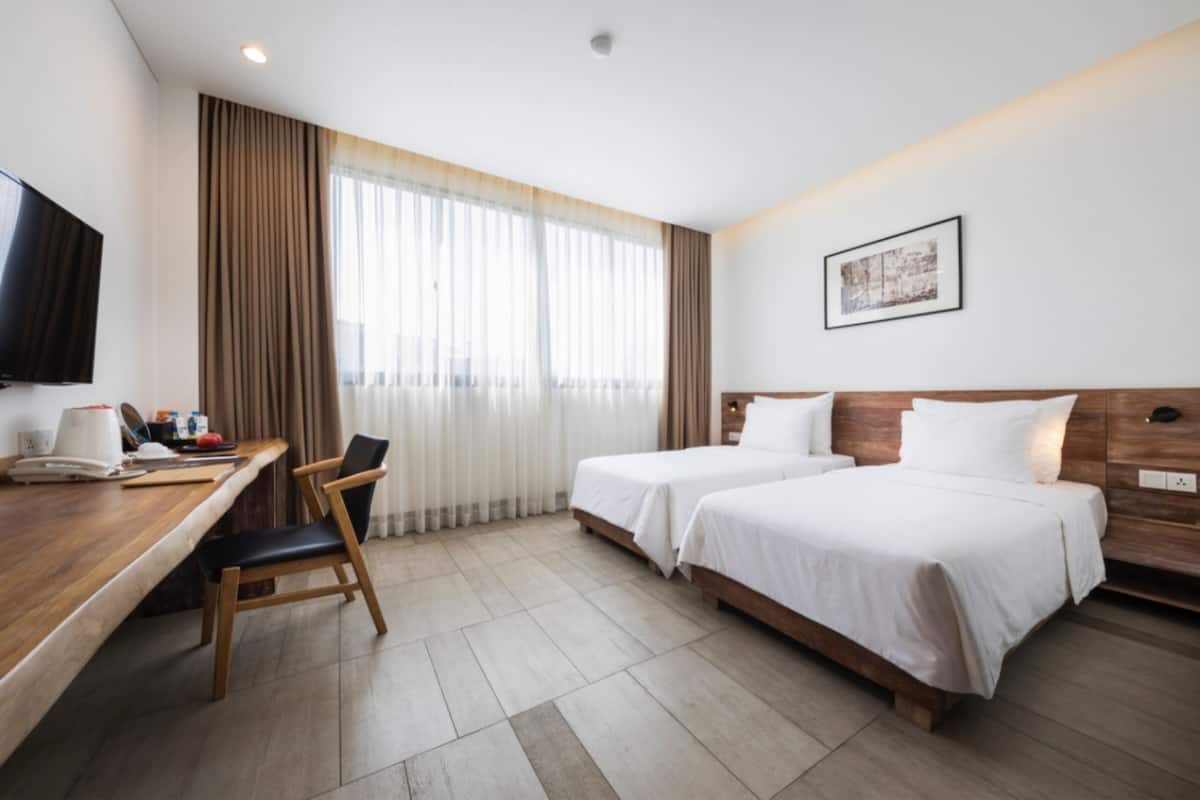 A hotel room with two beds, a desk, a chair, a television, and a window with curtains.