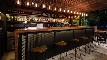 Un espace bar comprenant un comptoir de réception, des tabourets de bar et diverses bouteilles exposées sur des étagères.