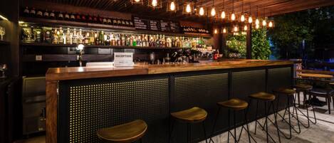 A bar area with a reception desk, bar stools, and a variety of bottles on shelves.