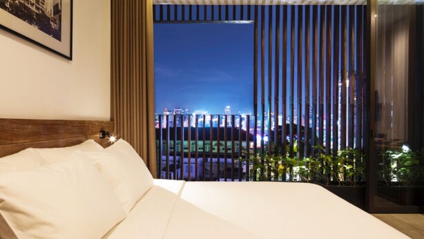A modern hotel room with a large bed, a city view through floor-to-ceiling windows, and a framed picture on the wall. - Triple E Hotel Fine Art Museum (Ho Chi Minh City)