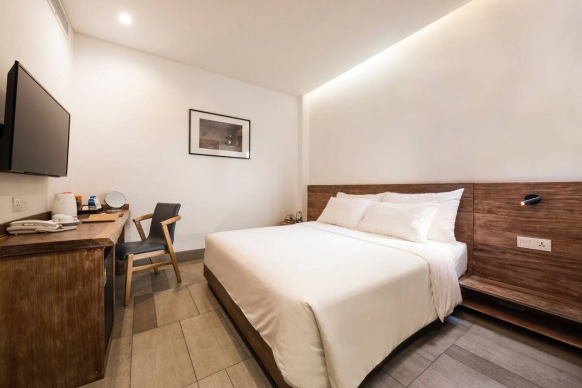 A hotel room with a bed, a desk with a telephone, a chair, a flat-screen TV mounted on the wall, and a framed picture on the wall.