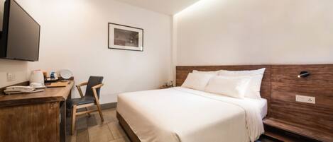 A hotel room with a bed, a desk with a telephone, a chair, a flat-screen TV mounted on the wall, and a framed picture on the wall.