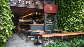 A restaurant with outdoor seating, a bar area, and a green wall. - Triple E Hotel Fine Art Museum (Ho Chi Minh City)