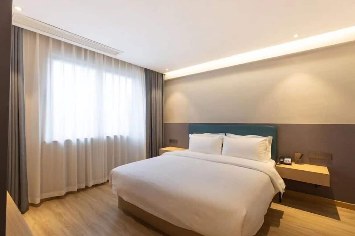 A hotel room with a large bed, a bedside table, a nightstand, and a window with curtains.
