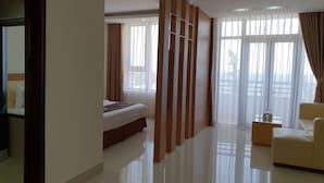 Ein Hotelzimmer mit einem Bett, einer Couch, einem Glastisch mit Flaschen und großen Fenstern mit Vorhängen.