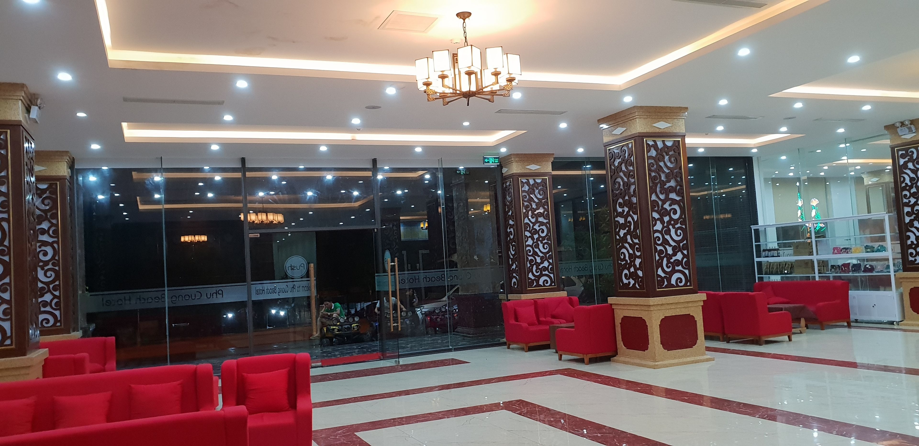 A spacious lobby with red seating, a chandelier, and a glass wall reflecting the interior.