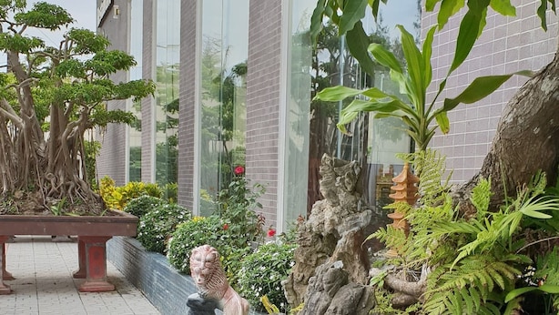 Ein friedlicher Garten mit Teich, einer Statue einer sitzenden Person und üppigem Grün.