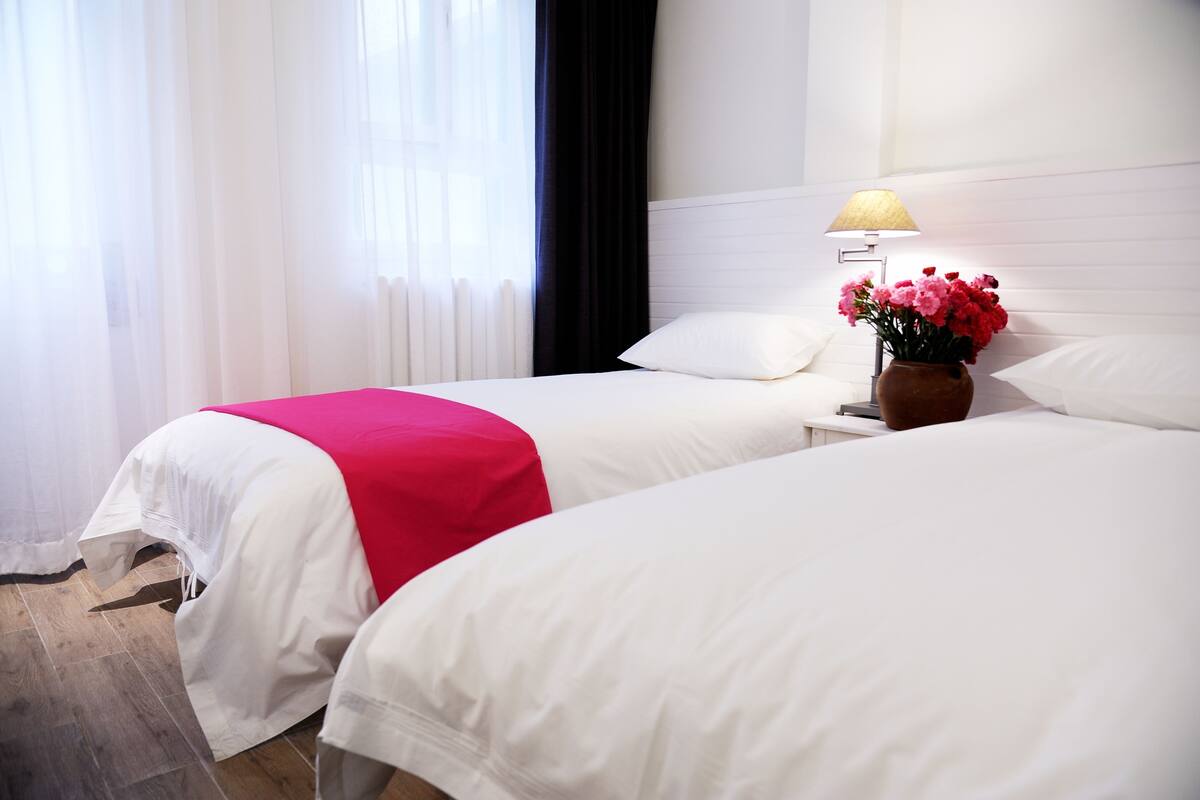 Habitación de hotel con dos camas, una mesita de noche con lámpara y un florero con flores.