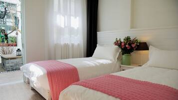 A hotel room with two beds, white bedding, a nightstand with a vase of flowers, and a view of the outside balcony.